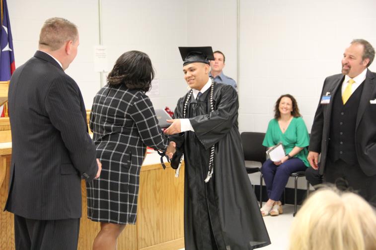 Youth inmate dressed in a black graduation cap and gown receiving his diploma.